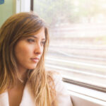 Young woman stares out of a train window as it's moving.